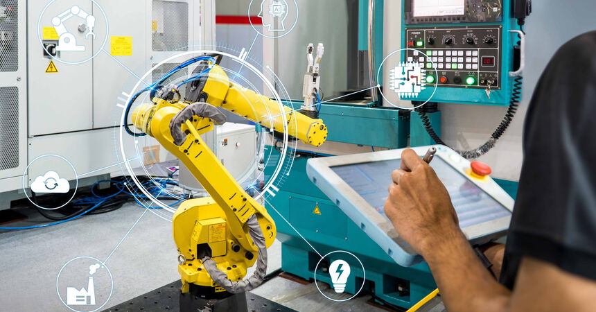 Person steuert einen Industrieroboter über ein Bedienpanel in einer digital vernetzten Produktionsumgebung.