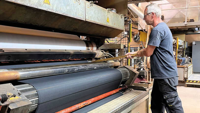 Fachkraft bedient eine industrielle Kaschiermaschine zur Verarbeitung von Stoffbahnen.