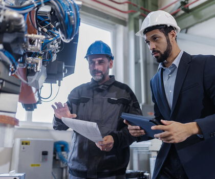 Zwei Mitarbeitende prüfen eine automatisierte Produktionsanlage und besprechen technische Abläufe in der Fertigung.