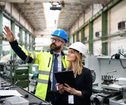 Zwei Mitarbeitende besprechen Produktionsprozesse und technische Anlagen in einer modernen Fertigungshalle.