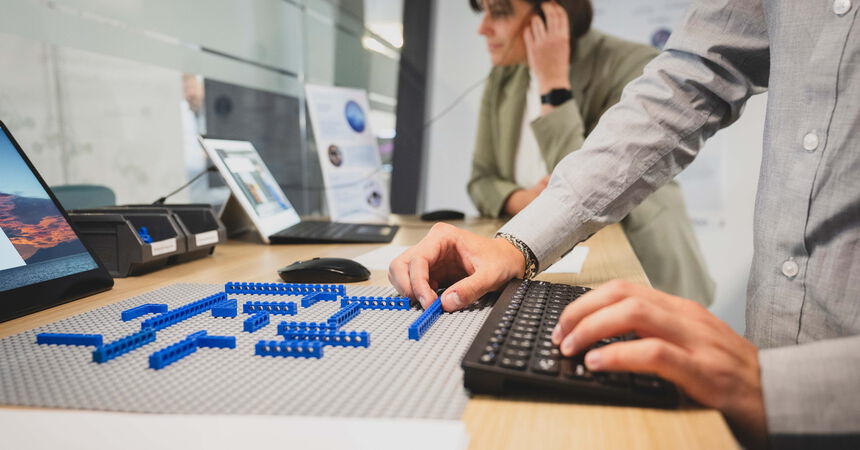 Person arbeitet mit Bausteinen und einer digitalen Anwendung an einem Arbeitsplatz zur Erprobung technischer Lösungen.