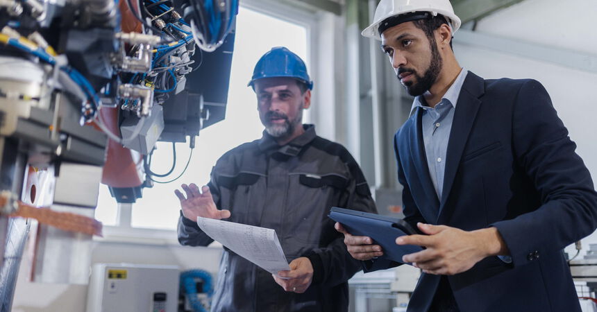 Zwei Mitarbeitende prüfen eine automatisierte Produktionsanlage und besprechen technische Abläufe in der Fertigung.