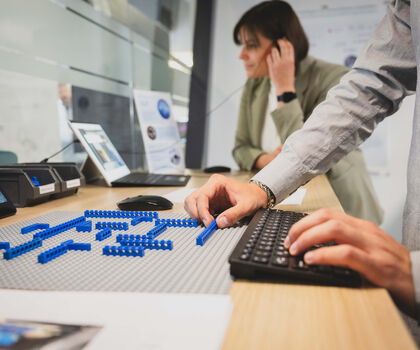 Person arbeitet mit Bausteinen und einer digitalen Anwendung an einem Arbeitsplatz zur Erprobung technischer Lösungen.