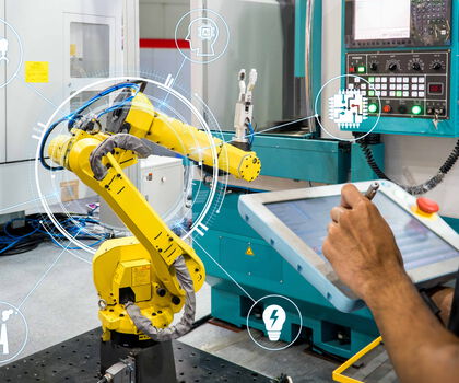 Person steuert einen Industrieroboter über ein Bedienpanel in einer digital vernetzten Produktionsumgebung.