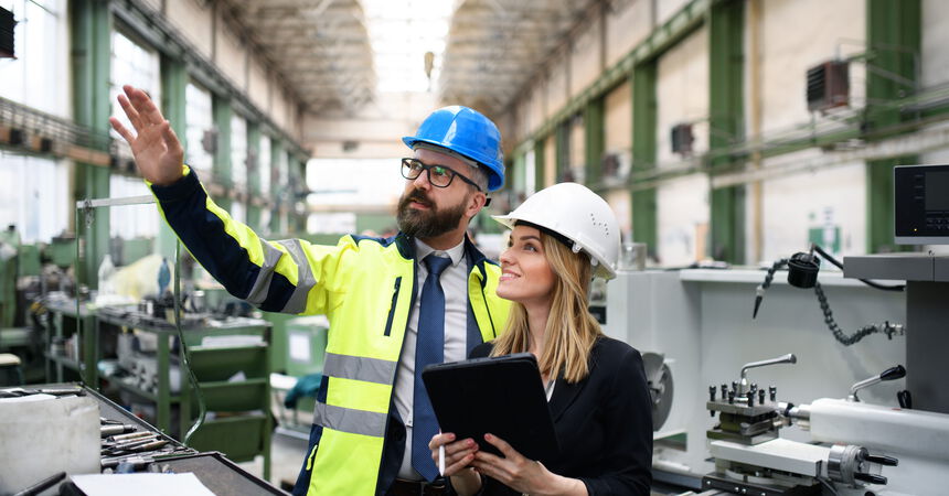 Zwei Mitarbeitende besprechen Produktionsprozesse und technische Anlagen in einer modernen Fertigungshalle.